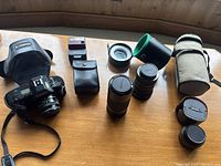 Full camera set displayed on table including Canon T70 camera with lens and strap, three lenses with caps and lens tubes, Canon 277 Speedlite flash, camera case, and manuals spread out.