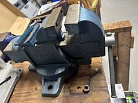 Blue cast iron bench vise mounted on wooden table, showing model number and design details