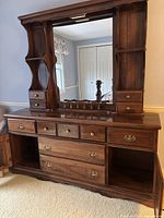 Front view of a dark wooden nine drawer dresser with an attached large mirror and carved supports; drawers have metal knobs and handles; dresser appears in lightly used condition.