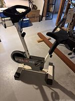 Side view of the CCM exercise bike in a basement setting, showing handle grips, seat, pedals, and base frame