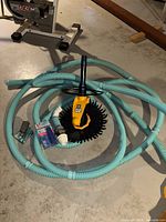 G2 Automatic Pool Cleaner with attached black cleaning brush, light blue hoses, Klear Sok, lubricant, and additional accessories laid out on concrete floor.