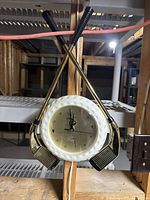 Photo of a golf-themed wall clock by Apollo brand with two crossed gold-tone golf club putters and a golf ball textured round white clock frame with gold face and black clock hands.