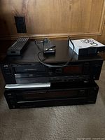 Front view of stacked JVC CD changer (top) and receiver (bottom) with remotes and cable on top