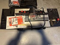 Top view of the benchtop router table with mounted plunge router, red adjustment knobs, power cord, and instruction manual visible.