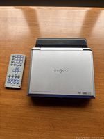 Closed Insignia portable DVD player with remote on wooden surface.