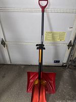 Full view of one snow shovel from the 3-piece set showing red and yellow blade and gray shaft with handle