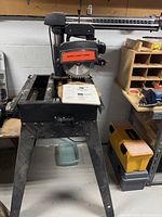 Radial arm saw on metal stand with blade and manual on top of base