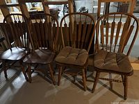 Set of four brown Windsor chairs including two with fabric seat cushions, showing overall style and condition in indoor setting.