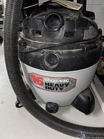 Front view of black and white Shop-Vac 16 gallon heavy duty wet/dry vacuum with attached black hose showing dust and dirt.