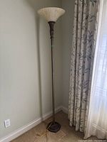 Full view of the standing floor lamp positioned near a wall and curtain, showing its entire height and design details.