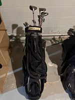 Full view of golf bag with clubs inside, showing left-handed notation taped on top, black golf bag with multiple compartments.