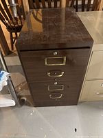 Front view of two drawer filing cabinet showing wood grain finish, brass hardware, and lock cylinders with no key.
