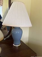 Photo of a vintage jar lamp with a blue ceramic base and beige large fabric shade on a wooden surface.