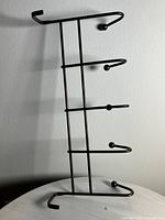Photo of a bronze metal wall hook rack with five hooks attached to a vertical frame, displayed on a table against a wall.