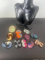 Photo displaying all 10 pairs of abstract mixed material dangle earrings arranged with a black mannequin bust.