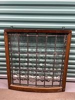 Full view of the stained glass cabinet window showing wooden frame and textured clear glass panels arranged in a grid pattern.