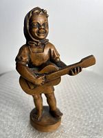 Front angle showing the girl smiling, holding the guitar, standing barefoot on base with natural wood finish.