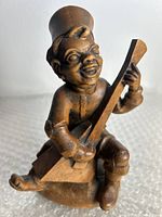 Front angle of the wooden hand carved boy figurine playing a stringed instrument, showing detailed carving and facial features.