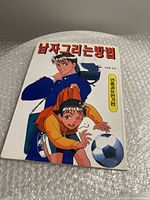 Front cover of Japanese art drawing book featuring anime-style young boys playing soccer, colorful illustration, minor wear.
