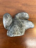 Top view of the dark green/gray soapstone sculpture showing rounded abstract forms resembling a bird shape.