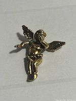 Close-up photo of the gold angel metal pin showing detailed wings, head, and body from front angle with the angel blowing a horn.