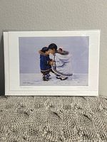 Front view of the art card in packaging showing the printed image of two Inuit-style figures in winter clothing with a snowy background.