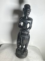 Full view of the standing wooden sculpture showing the figure playing the drum, highlighting overall form and proportions.