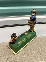 Photo showing the entire mechanical cast iron monkey bank with a standing figure holding a suitcase and a monkey pulling a lever on a green base.