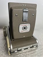 Front view of the closed Polaroid Land Camera showing textured metal exterior with Polaroid Land Camera logo plate and metal latch.