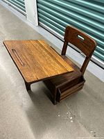 Front angle view showing the solid oak desk with integrated chair, tilt-top desk surface, and side book rack.