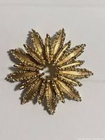 Front view of vintage gold tone flower brooch showing textured petals and open circular center, highlighting detailed craftsmanship.