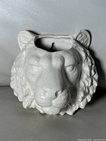 Front and side views of glossy white ceramic lion head wall decor showing detailed sculpting and mounting slot.