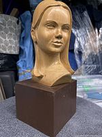 Side angle of wooden bust sculpture on a brown base in an indoor setting.