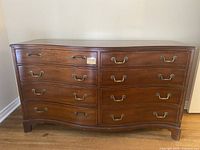 Front view of the 8 drawer wooden dresser showing curved left side drawers and brass handles.