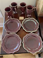 Four purple ceramic salad/dessert plates and four matching mugs arranged on a table showing the full set.