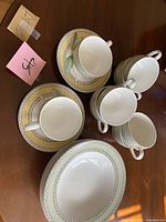 Top-down view of cups on matching saucers, alongside bowls with detailed geometric and leaf patterned borders in cream and yellow tones.