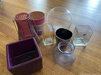 Photo showing 7 containers in various shapes and materials including purple glass, clear glass, and ceramic, placed on a wooden floor