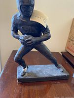 Front-right angle photo of the football player statue showing its running stance and flaking paint on foot and base.