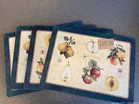 Set of four placemats stacked showing the fruit illustrations and blue border on top placemat.