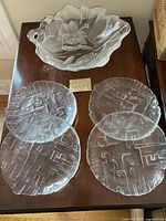 Full view of 7 textured glass plates and the floral glass bowl arranged on a wooden surface.