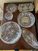 Top-down view of six Pinwheel crystal pieces showing detailed starburst and geometric cut patterns on glass plates, bowls, and trays.