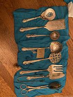 Photo of 9 silver color ornate utensils arranged on fabric showing details of each item