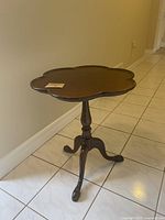 Full view of the small antique wooden table showing scalloped edge top and tripod base.