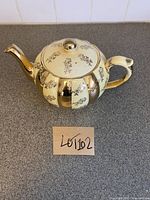 Photo of the whole teapot, showing yellow and gold vertical stripes with floral design, handle and spout detail