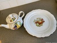 Teapot and plate side by side on counter, showing fruit designs and shape