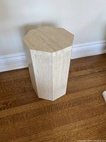 Full view of octagonal travertine pedestal stand on hardwood floor.