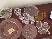 Various clear and amber glassware items including plates, bowls, and candle holders on wooden surface.