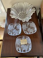 Three clear glass plates with raised narcissus flower design arranged around a larger fluted glass bowl with central floral design on a wooden table.