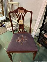 Front view of the antique wooden chair showing carved backrest and embroidered seat fabric.