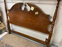 Wooden queen size headboard with curved top design and turned posts shown leaning against the wall.